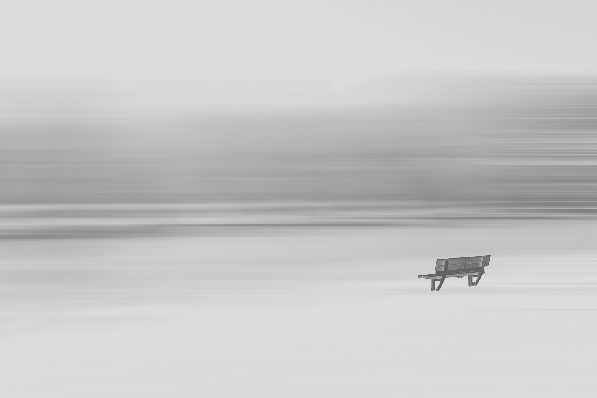 Holzbank in weiter, verschneiter Landschaft vor abstraktem, horizontal verschwommenem Hintergrund