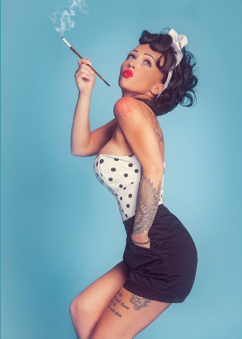 rau im Pin-up-Stil mit gepunktetem Top und Zigarettenspitze vor blauem Hintergrund.