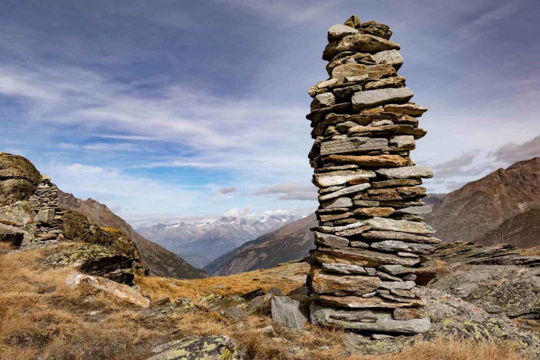 Hoher Steinhaufen (Cairn) in einem Gebirgstal mit schneebedeckten Gipfeln