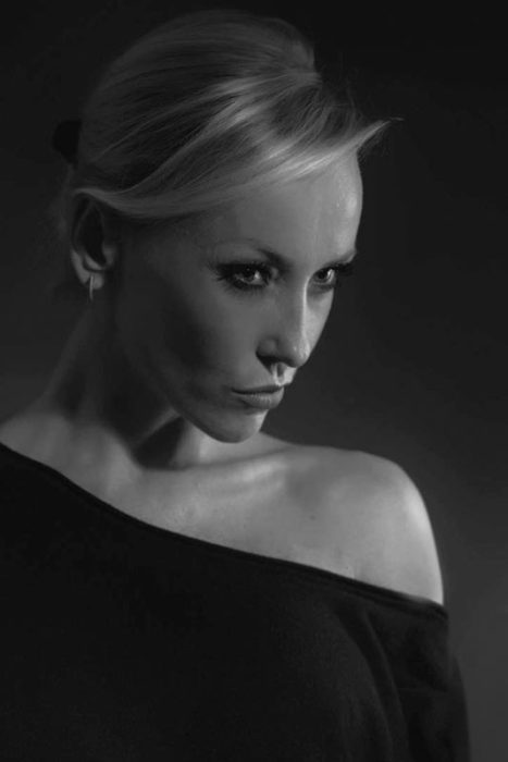 Schwarz-Weiß-Porträt einer Frau mit blonden Haaren, die zu einem Dutt zurückgebunden sind, und einem schulterfreien Oberteil, die zur Seite und leicht nach unten schaut.