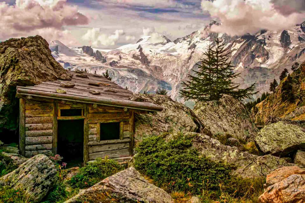 Rustikales Holzblockhaus in den Bergen mit schneebedeckten Gipfeln und Felsen