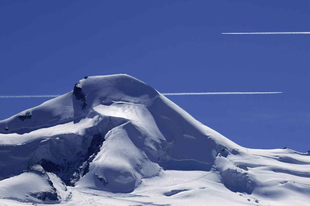 Schneebedeckter Berggipfel unter blauem Himmel mit zwei Kondensstreifen