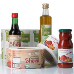 Produktetiketten für HUTH-Wuppertal, aufgerollt und als Flaschenetikett auf einer Glasflasche im Hintergrund.