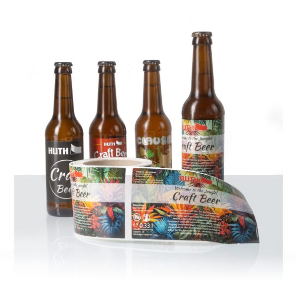 Dieses hochwertige Produktfoto demonstriert unsere Expertise als Etikettendruckerei. Es zeigt ein detailliertes Craft Beer Etikett im lebhaften "Welcome to the Jungle!" Dschungel-Design, angebracht auf einer braunen Bierflasche. Daneben präsentieren wir eine einzelne, abgelöste Etikette und eine große Rolle mit weiteren Etiketten, um die Qualität und den Umfang unserer Druckdienstleistungen zu veranschaulichen. Das Etikett besticht durch seine leuchtenden tropischen Farben, scharfe Details und enthält alle wichtigen Produktinformationen wie die Füllmenge (0,33 l). Perfekt für Brauereien, Getränkehersteller und Marken, die nach maßgeschneiderten, auffälligen und langlebigen Etikettenlösungen suchen. Wir bieten individuellen Etikettendruck für eine Vielzahl von Flaschen- und Verpackungsformaten.