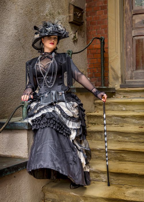 Frau in Steampunk-Kleid und Hut auf Treppe.