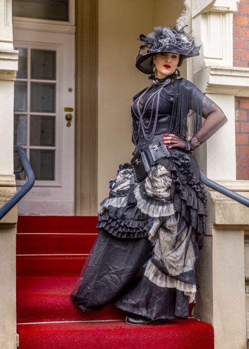 Frau im schwarzen Steampunk-Kleid auf rotem Teppich.