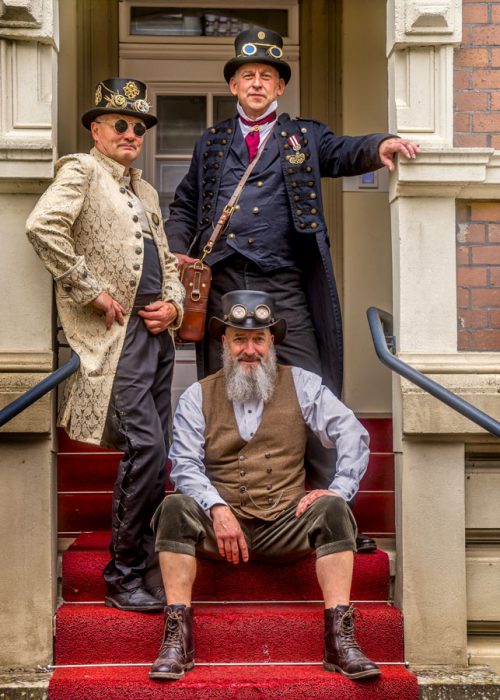Drei Männer in Steampunk-Kleidung auf roter Treppe.