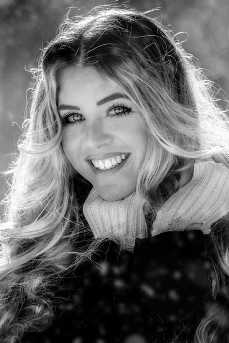 Schwarz-Weiß-Porträt einer lächelnden Frau mit langen Haaren und Schal im Winter.