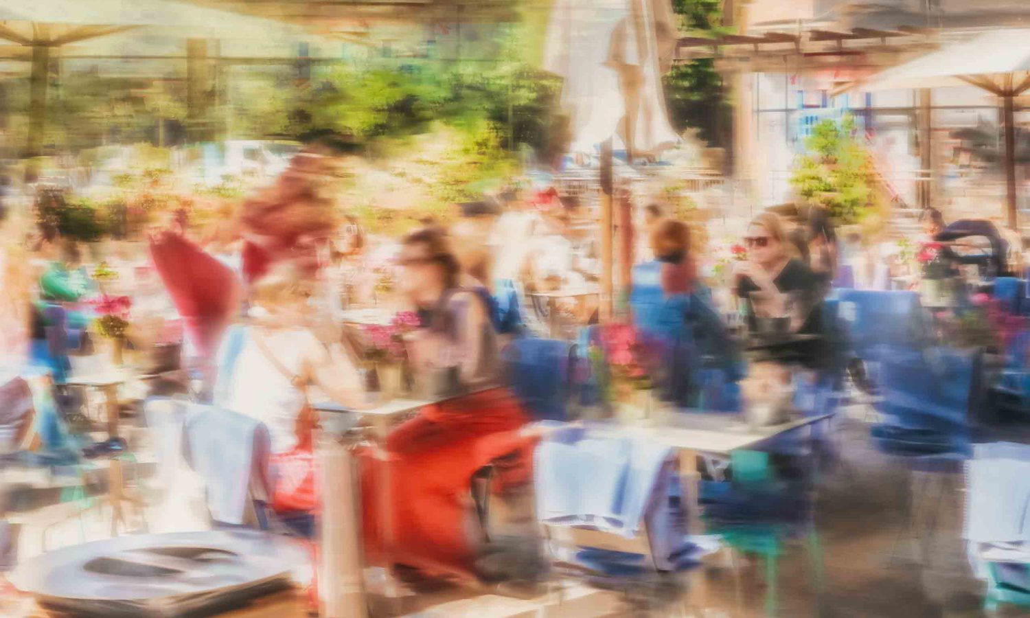 Künstlerische Straßenfotografie in ICM Wischtechnik – belebte Straßencafé Terrasse mit Menschen an Tischen unter Sonnenschirmen, bunte Farben und Bewegungsunschärfe im impressionistischen Stil.