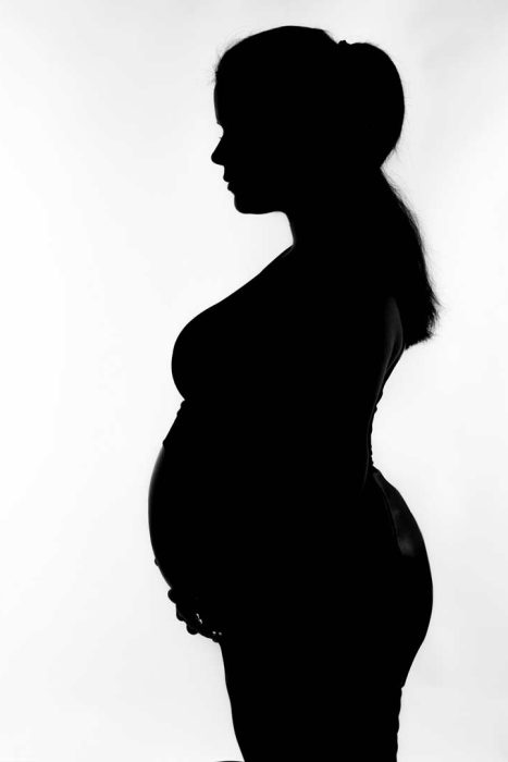 Schwarz-Weiß-Silhouette einer schwangeren Frau im Profil, die ihre Hände sanft auf ihren Bauch legt.