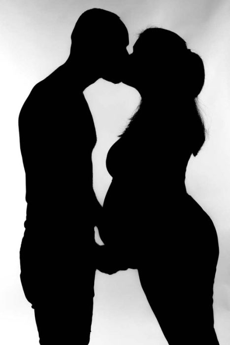 Schwarz-Weiß-Silhouette eines Mannes und einer deutlich schwangeren Frau, die sich innig küssen. Der Mann legt seine Hand sanft auf ihren Babybauch. Der Hintergrund ist weiß.