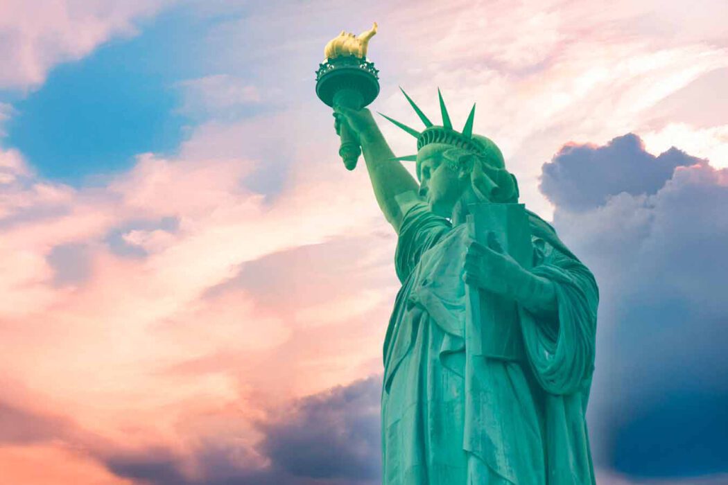Freiheitsstatue in New York mit erhobener Fackel vor dramatischem rosa-blauem Abendhimmel mit Wolken.