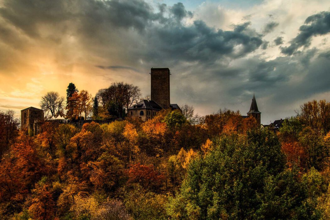Burg Blankenstein im Herbstwald bei dramatischem Himmel und Sonnenuntergang.