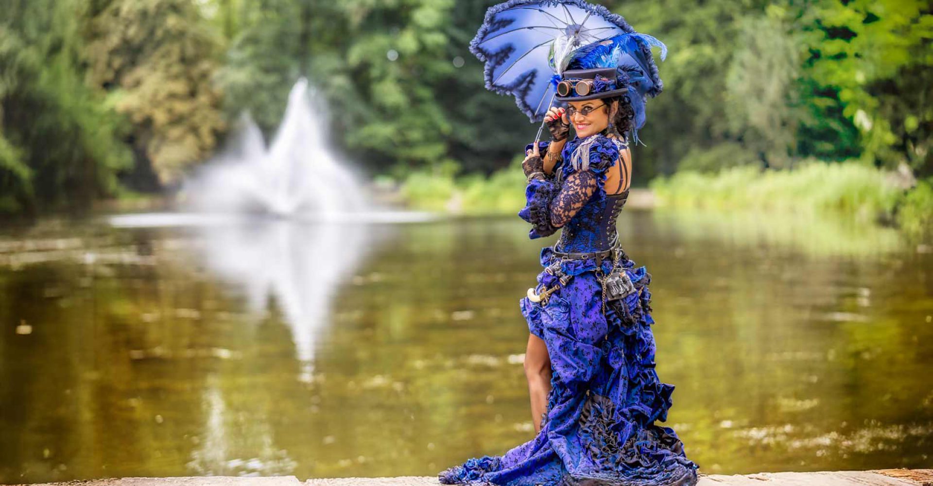 Frau in blauem Steampunk-Kleid mit Schirm am See.
