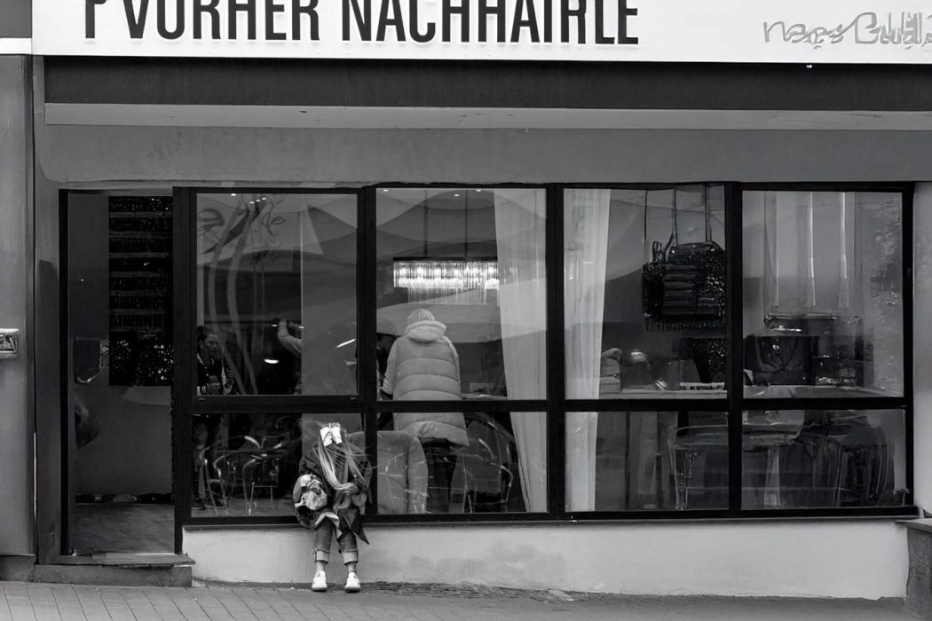 Geschäftsportal Schwarz-Weiß mit sitzender Person und Schaufenster. Streetfotografie
