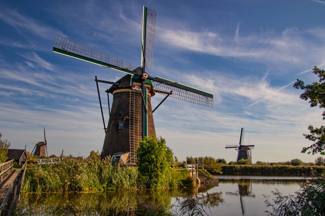 Traditionelle holländische Windmühle an einem Flusslauf bei sonnigem Wetter mit blauem Himmel und leicht gewölkten Schleierwolken.