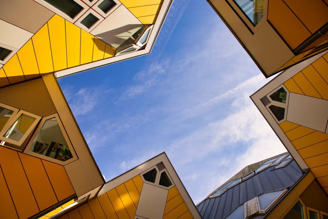 Perspektivische Aufnahme der gelben Kubushäuser in Rotterdam mit Blick nach oben auf die markanten, schräg geneigten Fassaden und den blauen Himmel.