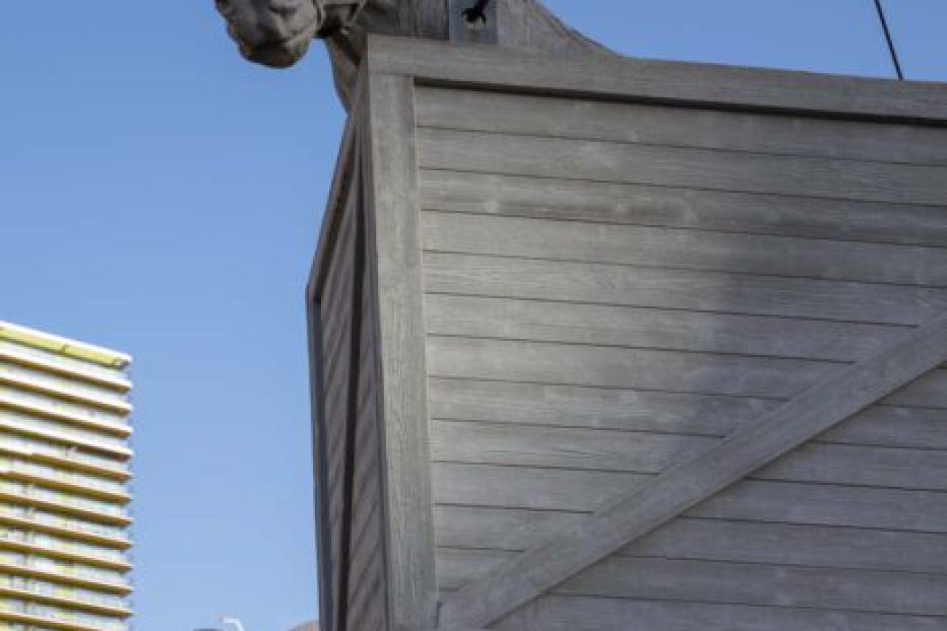Skulptur eines Pferdes auf einem hölzernen Lastenträger vor der modernen Stadtkulisse von Rotterdam unter blauem Himmel.