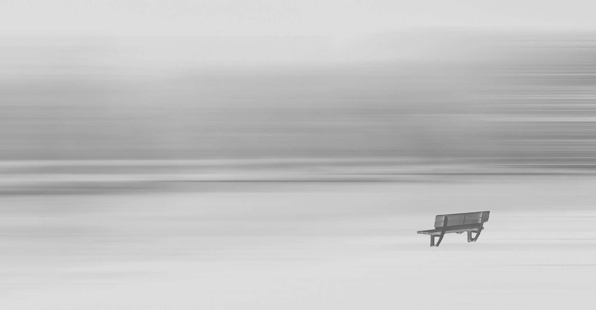 Holzbank in weiter, verschneiter Landschaft vor abstraktem, horizontal verschwommenem Hintergrund