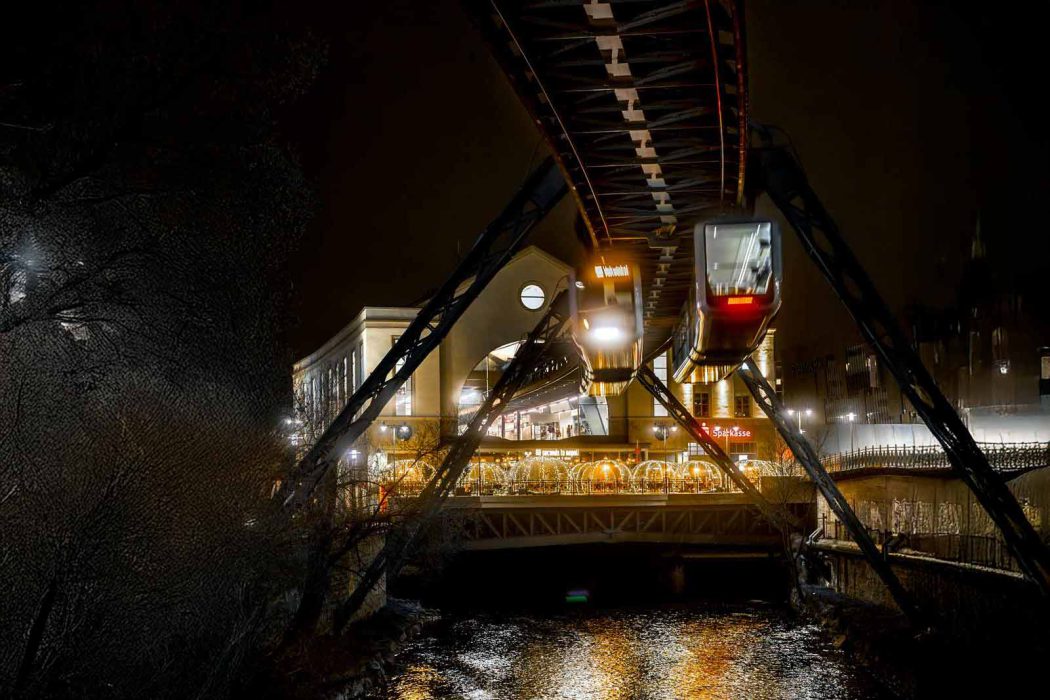 Wuppertaler Schwebebahn bei Nacht über einem Fluss mit beleuchteten Zügen.