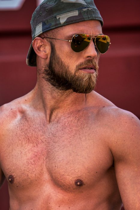 Muskulöser Mann mit blondem Bart, Camouflage-Mütze und goldener Sonnenbrille