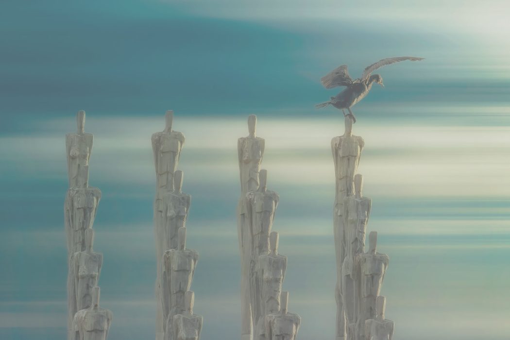 Surreale Skulpturen aus gestapelten menschlichen Formen mit einem Vogel auf der Spitze vor himmelartigem Hintergrund