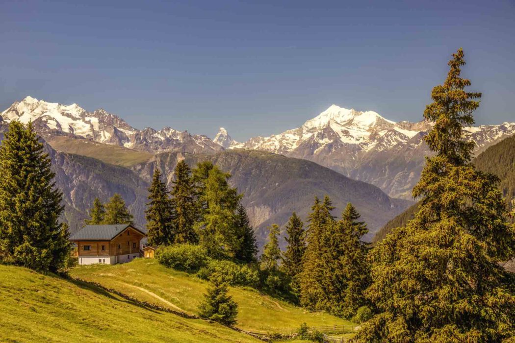 dyllische Alpenlandschaft mit Holzhaus, Bäumen und schneebedeckten Bergen