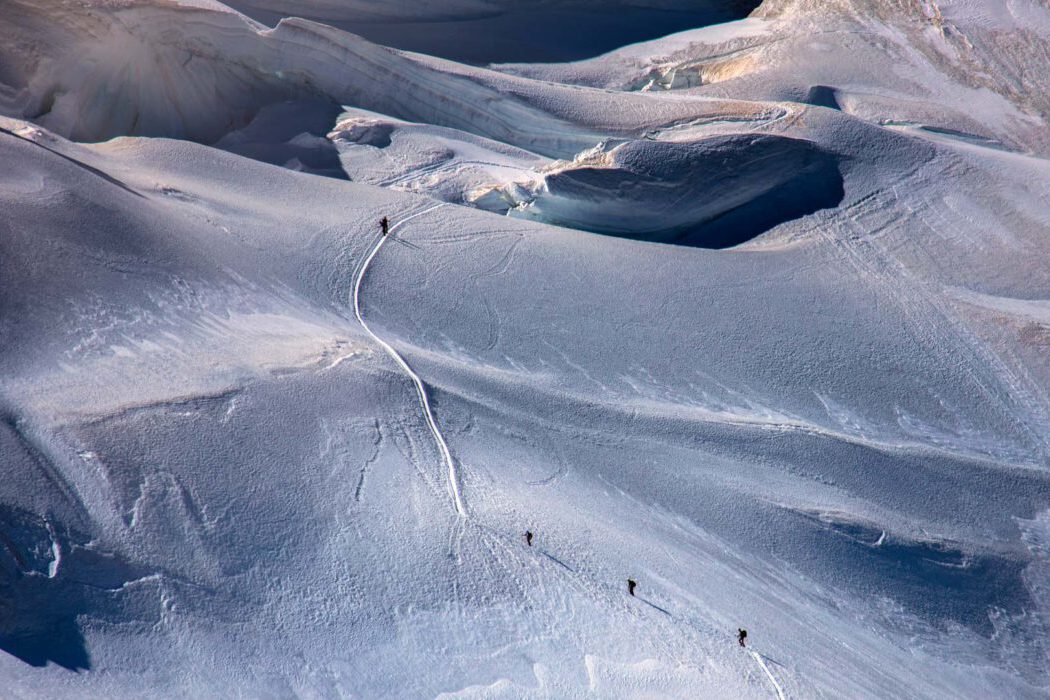 Luftaufnahme von Bergsteigern, die eine Schneespur in den Alpen hinaufsteigen, mit Spuren im Schnee.